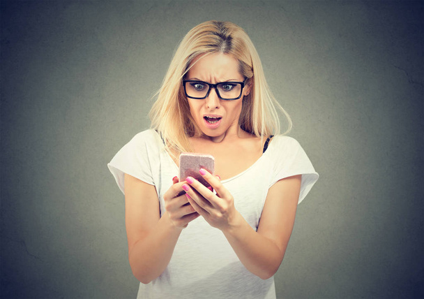 Shocking message. Surprised blond hair woman holding mobile phone and staring at it  - Fotoğraf, Görsel