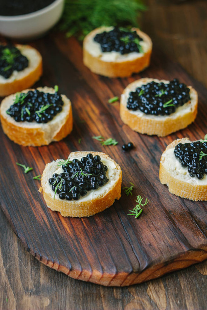 Black caviar on the pieces of bread over wooden kitchen board. - Fotografie, Obrázek