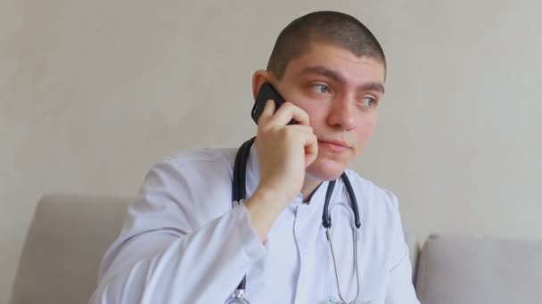 Good doctor guy on mobile gives advice to patients sitting on couch in office of hospital. - Záběry, video