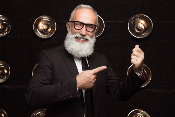 Happy old attractive business man points with a finger at the money. Empty space for money. Bearded man show how he holding money in the suit  - Foto, Imagem