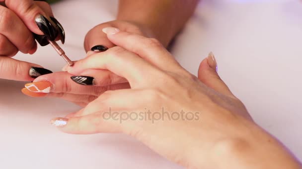 De manicure dekt de vrouw vingernagel op de middelvinger van haar linkerhand met een bruin lak. - Video