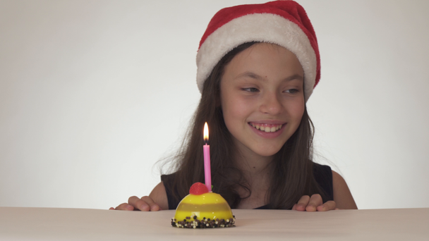 Mooie Stout meisje tiener in Kerstman hoed blaast in het geheim kaars op feestelijke taart op witte achtergrond stock footage video - Video