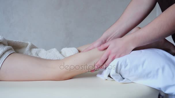Professionale massaggiatore maschile impasta le gambe della paziente ragazza, che si trova sul divano in ufficio luminoso
. - Filmati, video