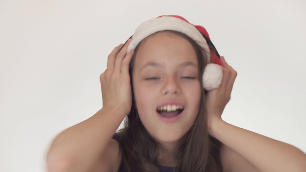 schöne freche Teenagerin mit Weihnachtsmann-Hut hört Musik über Kopfhörer und singt auf weißem Hintergrund mit. - Filmmaterial, Video