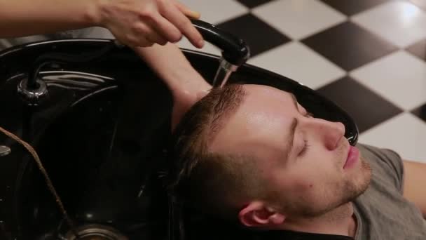 Женщина моет голову в парикмахерской бородатому мужчине с шампунем и кондиционером. Смой шампунь с воды.
. - Кадры, видео