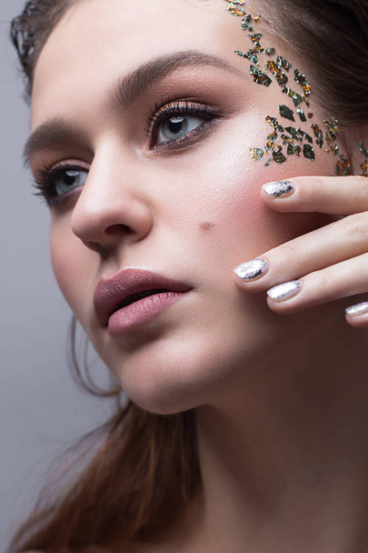 A young girl with a gentle classical make-up and loose hair. Beautiful model with creative art make-up and manicure from foil. Beauty of face and shining skin.  - Foto, imagen