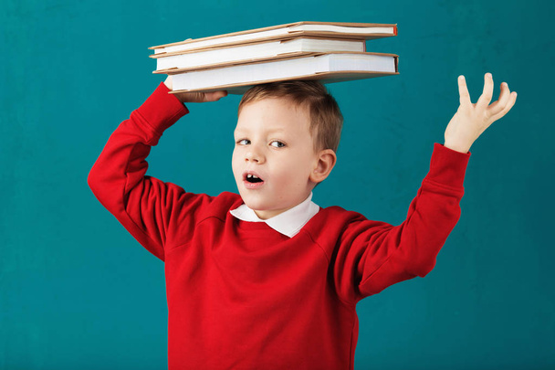 Vrolijke glimlachend jongetje met grote boeken op zijn hoofd in de school ha - Foto, afbeelding
