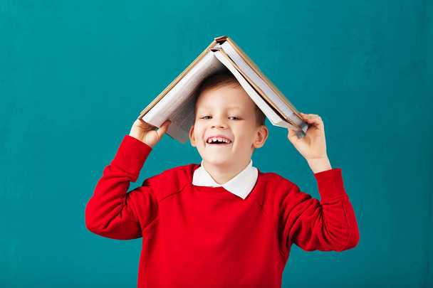 fröhlich lächelnder kleiner Schuljunge mit großen Büchern auf dem Kopf ha - Foto, Bild