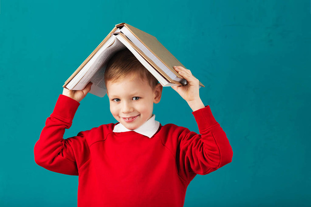 Wesoły, uśmiechnięty chłopczyk szkoły z duże książki na głowie ha - Zdjęcie, obraz