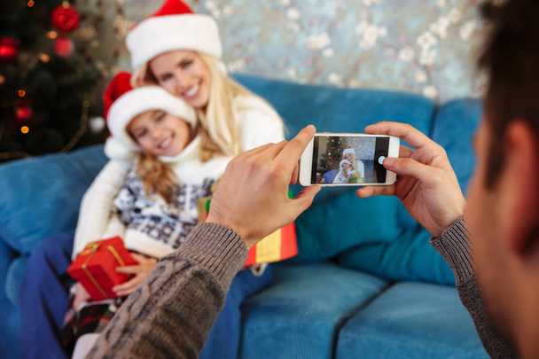 Father taking photo of his cheerful wife and daughter in Santa's - Fotoğraf, Görsel
