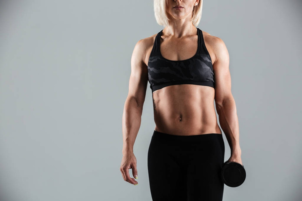 Cropped image of a muscular sportswoman holding dumbbell - Zdjęcie, obraz