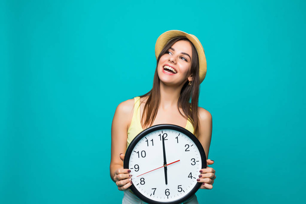 junge glückliche Frau in der Hand eine Uhr mit 12 Uhr auf grünem Hintergrund. Porträt einer positiven hübschen jungen Frau mit Wanduhr vor weißem Hintergrund - Foto, Bild