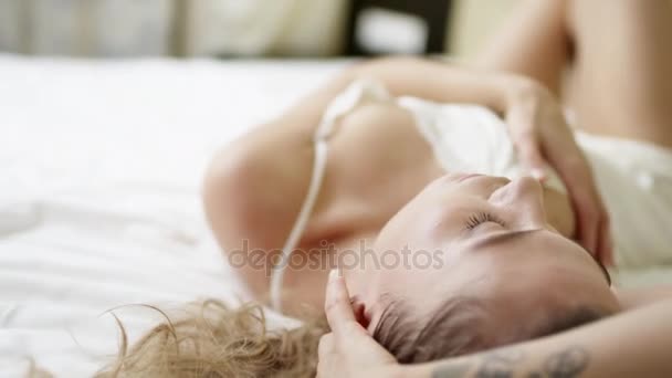Seksowna młoda kobieta, pozowanie na łóżku leżąc na plecach i głaszcząc jej podbrzusze - Materiał filmowy, wideo