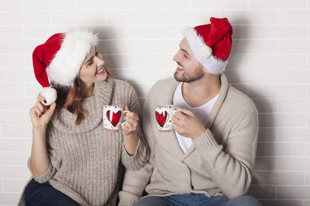 Улыбающаяся пара в Санта-шляпе и рождественской чашке
. - Фото, изображение