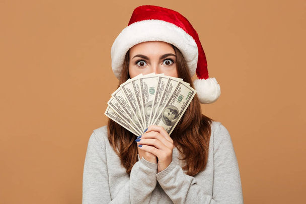 Caucasian shocked lady wearing christmas hat holding money. - Foto, afbeelding