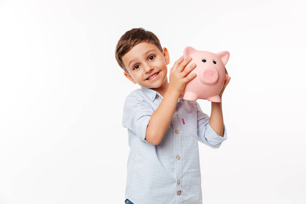 Portrait of a joyful cute little kid holding piggy bank - Фото, зображення