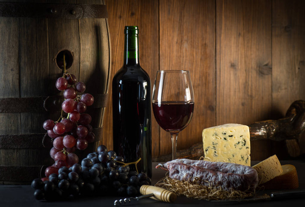 Glass of red wine cheeses grapesand barrel on brown wood - Foto, afbeelding