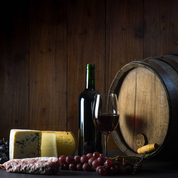 Glass of red wine cheeses grapesand barrel on brown wood - Photo, Image
