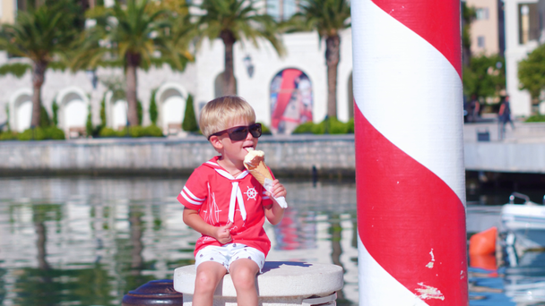 Zbliżenie małego chłopca z okulary jedzenie lodów w marina - Materiał filmowy, wideo