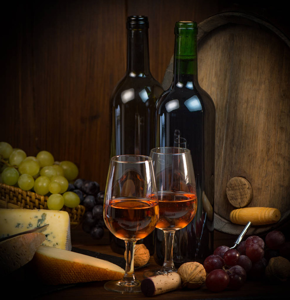 Glasses of rose wine cheeses grapesand barrel on brown wooden background - Fotó, kép