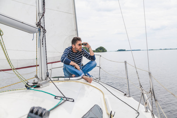 man sits on sailing yacht and looks through binoculars - Photo, image