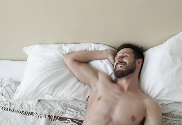 Carefree guy enjoying new day. Sexy, happy bearded man in bed. - Фото, зображення
