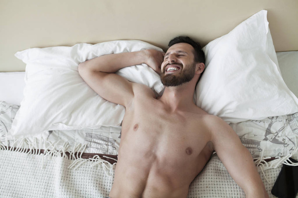 Carefree guy enjoying new day. Sexy, happy bearded man in bed. - Photo, Image