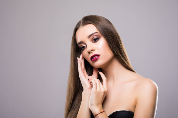 Pretty girl with big eyes and dark eyebrows, with naked shoulders, looking at camera and smiling, a model with light nude make-up, gray studio background, beauty photo, copy space, close up. - Foto, Imagem