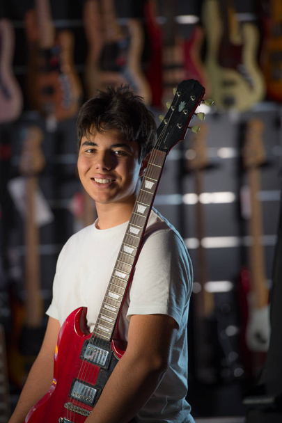 Happy teenage boy choosing acoustic guitar in musical shop - Фото, изображение