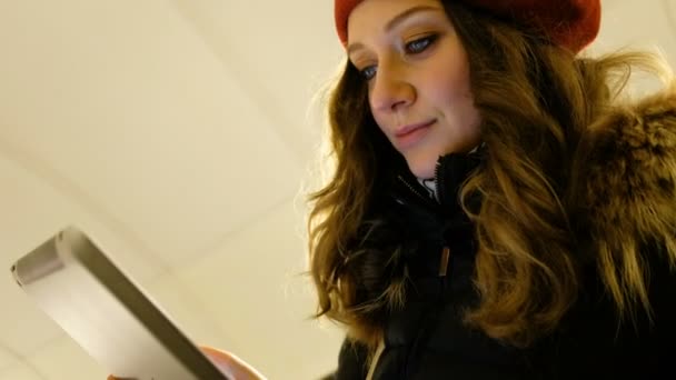 Detailní záběr na atraktivní dívka s tabletem v ruce po eskalátoru v metru, při pohledu na dotykové obrazovce a pohyblivé prsty po obrazovce - Záběry, video