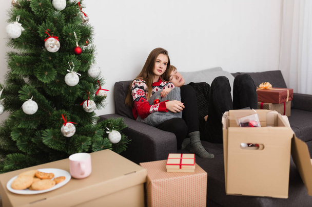Foto de una hermosa pareja joven sentada en el sofá en casa mientras pasan tiempo juntos con el árbol de Navidad cerca
 - Foto, imagen