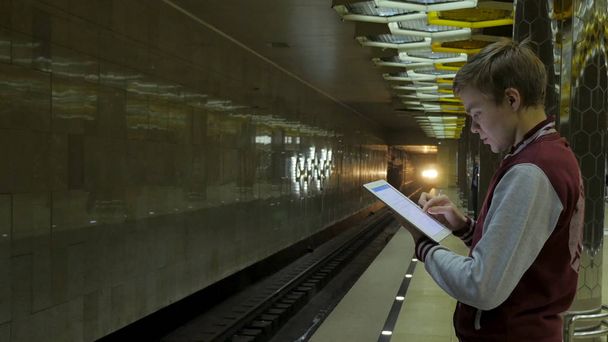 Людина за допомогою сенсорною панеллю або смартфон, коли він чекає поїзда на станцію метро. За допомогою бездротової цифрової планшетному ПК в поїзді, залізничним або станції метро в сучасному місті бізнесмен - Фото, зображення