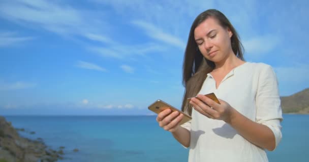 Woman using credit card on vacation shopping online with mobile phone at clear blue sea background - Materiał filmowy, wideo