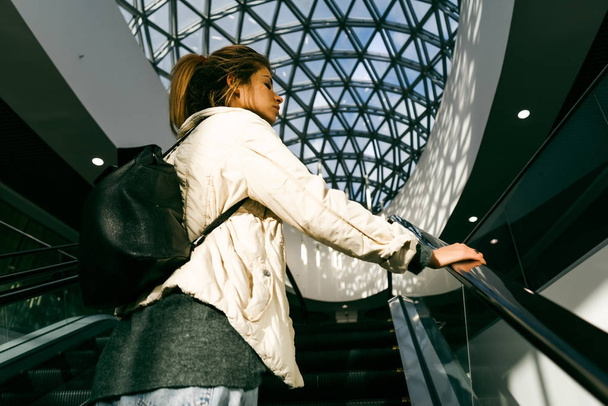 stylish blonde girl rises up on an escalator, in a mall - Zdjęcie, obraz