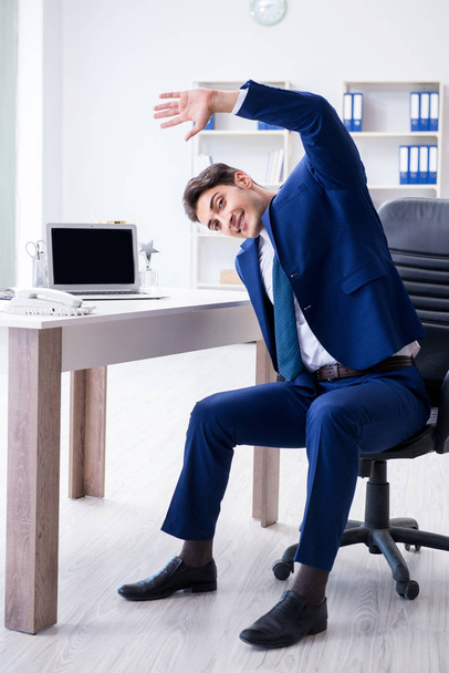Giovane uomo d'affari che fa sport stretching sul posto di lavoro - Foto, immagini