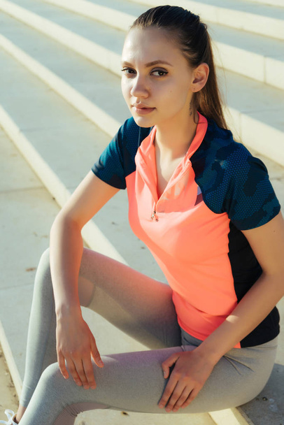 joven chica de fitness en ropa deportiva descansando después de trotar en los pasos, mirando a la cámara
 - Foto, imagen