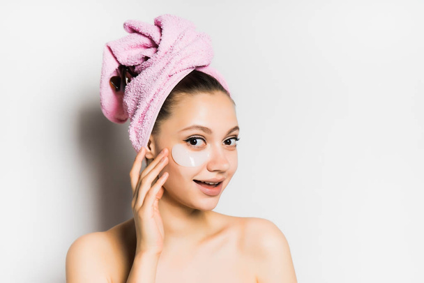 happy young girl with clean skin, pink towel on her head, silicone patches under eyes looking at camera, smiling - Fotó, kép