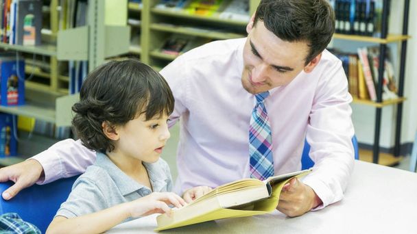 Учитель и мальчик учатся с книгой на книжной полке
 - Фото, изображение