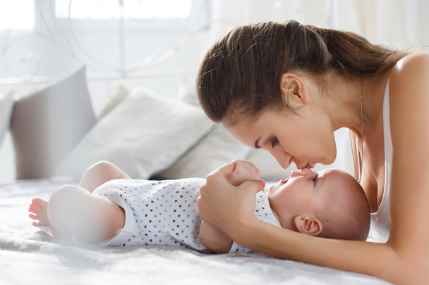 Young mother lying in bed with her newborn baby boy, playing together, happiness family concept, kid and mom bonding.Beautiful young mom looking at her baby son and smiling, lying in bed at home - Foto, Bild