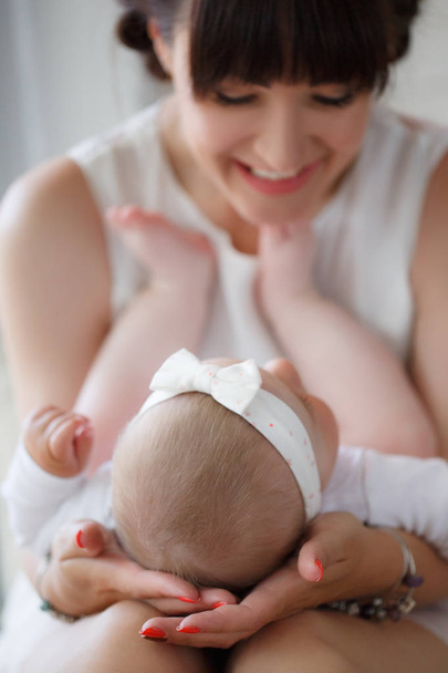 Στην αγκαλιά του μια ευτυχισμένη μητέρα ντυμένος με ένα ροζ πουκάμισο και μπλε τζιν βρίσκεται ένα νεογέννητο μωρό, για τον καθορισμό λίγο τα πόδια της στο στήθος της μητέρας, η μητέρα υποστηρίζει απαλά το κεφάλι του παιδιού με τις παλάμες των χεριών της, μια ευτυχισμένη οικογένεια - Φωτογραφία, εικόνα