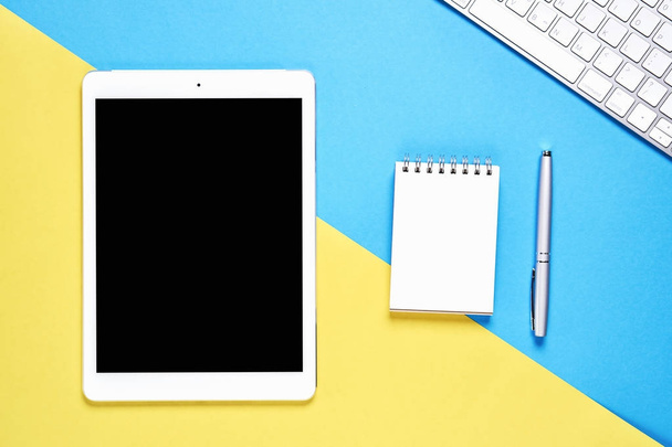 schwarzer Bildschirm Tablet leer und Notizbuch auf pastellgelbem und blauem Hintergrund platziert. geeignet für Grafiken, die für Werbung verwendet werden. - Foto, Bild