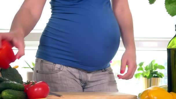 Chica embarazada del estómago y las manos rebanando fruta de pimentón rojo con cuchillo para ensalada
 - Metraje, vídeo