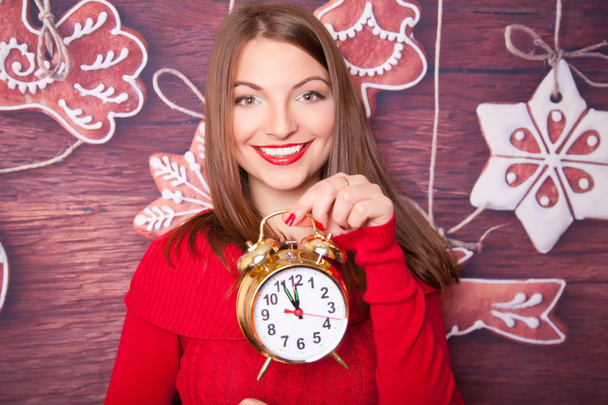 Bastante joven chica usando rojo vestido de punto de pie con reloj de oro que muestra cinco a doce
 - Foto, Imagen