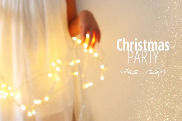 Abstract and bokeh image of young woman holding garland christmas lights and typography: CHRISTMAS PARTY. Holiday invitation concept. - Фото, зображення
