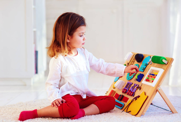 cute baby girl having fun playing with colorful wooden busy board - Foto, afbeelding