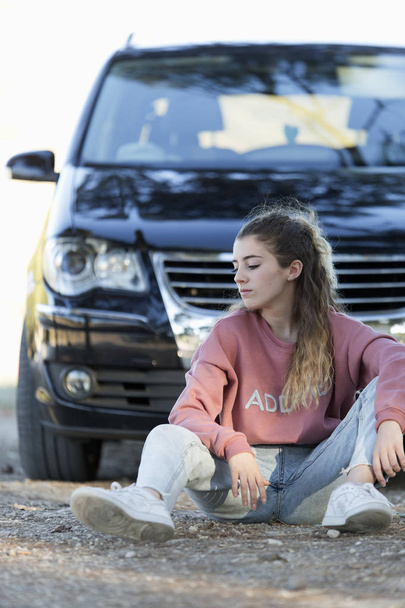 Teenager sitting on the floor in front of a car - Φωτογραφία, εικόνα