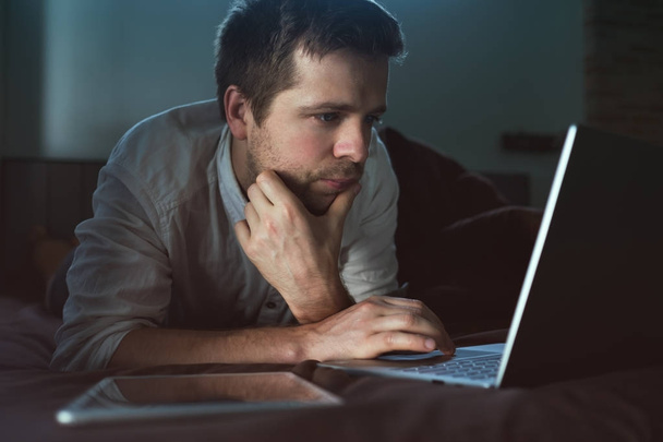 Kavkazská mladý muž ležel na posteli v jeho laptopu. Práce doma. - Fotografie, Obrázek