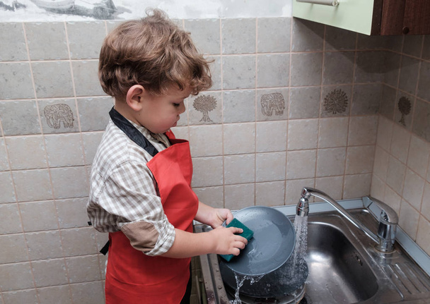 Europejskiego chłopiec zmywa naczynia w domu - Zdjęcie, obraz