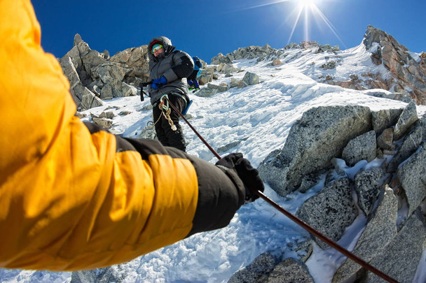 Tied climbers climbing mountain with snow field tied with a rope with ice axes and helmets first person - Fotó, kép