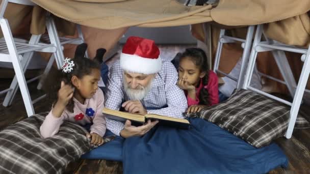 Дедушка в шляпе Санты читает книгу с детьми
 - Кадры, видео